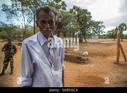 10. April 2015 - Jaffna-Halbinsel, Sri Lanka - Ein Militärbüro aus Sri Lanka überblickt einen tamilischen Mann Murugesan, der auf die Freilassung seines Hauses im Bezirk Valikamam, Sri lanka, wartet. Das Land wurde während des 26-jährigen Konflikts geräumt und später gegen Ende des Konflikts vom srilankischen Militär besetzt. (Bild: © Amrita Chandradas Via ZUMA Wire) Stockfoto