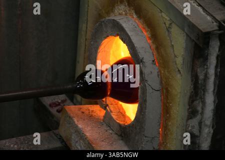 Ein Handwerker erhitzt mundgeblasenes Glas in einem Ofen, um eine wunderschöne Vase herzustellen. Stockfoto