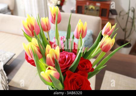 Farbenfroher Blumenstrauß aus Tulpen und roten Rosen in gemütlicher Innenatmosphäre Stockfoto