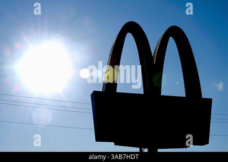 Die Sonne beleuchtet an einem sonnigen Tag ein McDonald's Fast-Food-Restaurant-Schild. Stockfoto