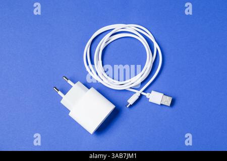 USB-Netzteil und Ladekabel auf blauem Hintergrund, flach verlegt Stockfoto
