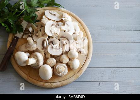 Frische Knopfpilze ganz und in Scheiben geschnitten, Petersilie isoliert auf grauem hölzernem Hintergrund. Genießbare Champignonpilze. Vegetarische, vegane und gesunde Lebensmittel. Stockfoto