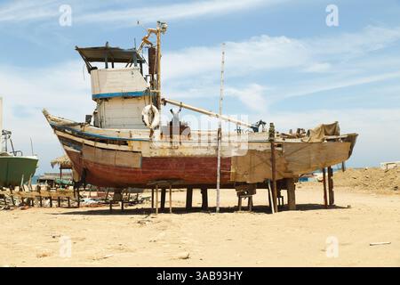 Ein verlassenes hölzernes Fischerboot befindet sich am Sandstrand von Mancora, Peru, das von der Zeit und der salzigen Meeresbrise verwittert ist. Eine nostalgische Erinnerung an das t Stockfoto
