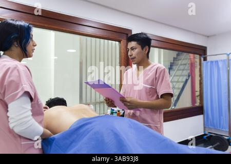 Physiotherapeuten in einer ecuadorianischen Klinik bieten eine personalisierte Betreuung. Das Team, in rosa Peelings gekleidet, konzentriert sich auf die Rückenbehandlung eines Patienten, Promot Stockfoto