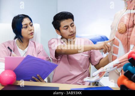 Zwei Physiotherapiestudenten in Ecuador nehmen an einer Studienzeit Teil, um anatomische Strukturen zu untersuchen. Sie tragen pinke Uniformen und konzentrieren sich auf eine Deta Stockfoto
