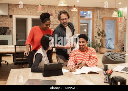 Ein vielfältiges Team arbeitet energisch in einem modernen Coworking-Raum zusammen. Das warme Ambiente und die kreative Umgebung fördern Teamarbeit und Innovation Stockfoto