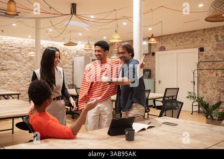 Eine Gruppe von Fachleuten interagiert freudig in einem modernen Coworking-Raum, um Kreativität und Zusammenarbeit zu fördern. Das Setting hebt Teamwork und Profi hervor Stockfoto