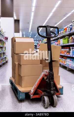 Ein beladener Lagerwagen befindet sich in einem Supermarktgang, auf dem Kartons gestapelt sind. Die Regale sind mit verschiedenen Produkten ausgekleidet, wodurch r Stockfoto