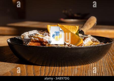 Serviert österreichischer Kaiserschmarrn, ein geriebener Pfannkuchen, mit Puderzucker bestäubt und mit frischen Orangenscheiben in einer gusseisernen Pfanne begleitet. Stockfoto