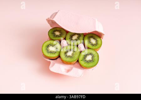 Von oben sind frische Kiwi-Scheiben ordentlich in einem rosafarbenen Eierkarton angeordnet, was eine nahrhafte und kreative Alternative zu traditionellen Ostereiern darstellt. Stockfoto