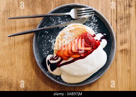 Genießen Sie flauschige japanische Pfannkuchen mit frischen, saftigen Erdbeeren und einem Klecks Schlagsahne. Mit Sirup getränkt und mit Zucker bestäubt, pe Stockfoto