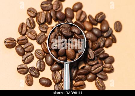Eine Nahaufnahme der gerösteten Kaffeebohnen, die auf einer Oberfläche verstreut sind. In der Mitte befindet sich ein Metalllöffel, der mit Bohnen gefüllt ist und deren Textur und unterstreicht Stockfoto