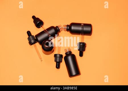 Schwarze Tropfflaschen auf einem leuchtend orangefarbenen Hintergrund, ideal für die Präsentation von Kosmetik, ätherischen Ölen oder Hautpflegeprodukten mit einem modernen und Stockfoto