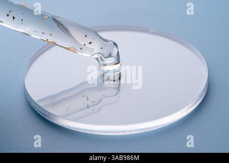 Makrofoto einer kosmetischen Pipette, die eine transparente, gesprenkelte Flüssigkeit mit goldenen Partikeln auf eine Petrischale aus Glas tropft und dabei Präzision und Puri zeigt Stockfoto