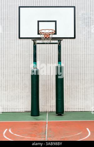 Basketballplatz im Freien in Hongkong, mit einem Basketballkorb mit weißem Fliesenboden und einem Netz, der an einer Wand mit gemusterten Fliesen angebracht ist. Das Feld wird angezeigt Stockfoto