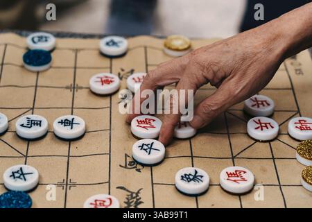 Zugeschnittene Nahaufnahme der Hand eines nicht erkennbaren älteren Menschen, die selektiv Fliesen auf dem chinesischen Brettspiel Xiangqi in Hongkong platziert Stockfoto