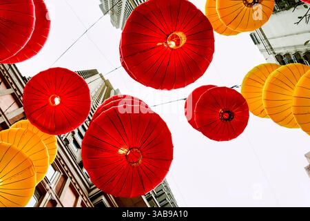 Von unten leuchtende rote und gelbe Laternen, die während der Feier des chinesischen Neujahrs zwischen Gebäuden in Hongkong hängen und die traditionelle Stockfoto