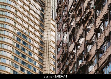 Dieses Bild fängt einen beeindruckenden Kontrast zwischen eleganter, moderner Architektur und einem alten Wohngebäude in Hongkong ein und unterstreicht das vielfältige urba Stockfoto