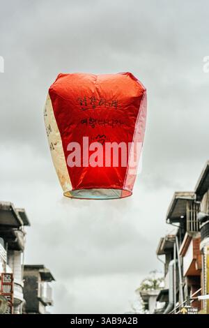Eine rote chinesische Papierlaterne erhebt sich gegen einen bewölkten Himmel, verziert mit handgeschriebenen Glücksphrasen in schwarzer Tinte. In Taiwan, diese traditionelle Laterne Stockfoto