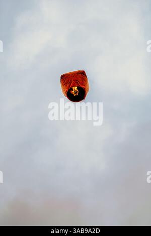 Von unten eine orange chinesische Laterne, die gegen einen bewölkten Himmel in Taiwan fliegt. Die Laterne trägt Wünsche und Segnungen, die aus einem niedrigen Winkel gefangen werden. Stockfoto