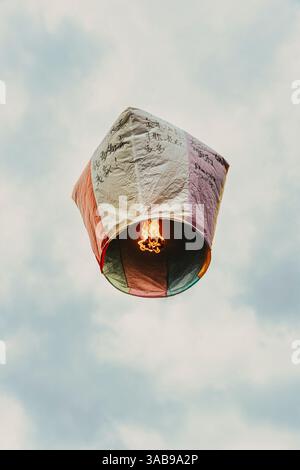 Von unten schwebt chinesische Papierlaterne in Taiwan vor einem bewölkten Himmel, geschmückt mit handgeschriebenen traditionellen Segnungen für Gesundheit, Glück und Profis Stockfoto