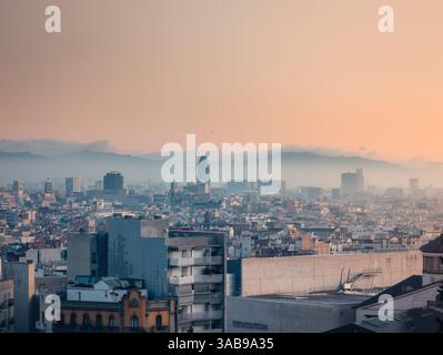 Ruhiger Blick auf Barcelona bei Sonnenaufgang, zeigt die Stadtlandschaft mit berühmten Wahrzeichen unter einem weichen, leuchtenden Himmel, mit nebelbedeckten Bergen im bac Stockfoto