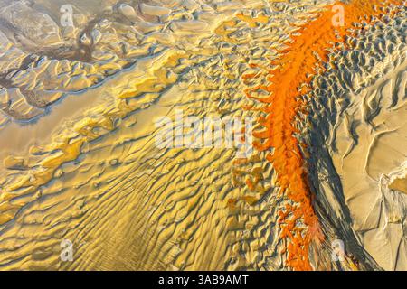 Luftbild mit markanten orangen und gelben Sandmustern, die an Wellen an einem Strand erinnern und eine faszinierende natürliche abstrakte Kunst schaffen. Ideal für B Stockfoto