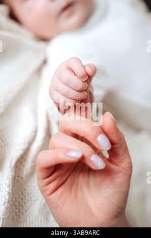 Ein Nahaufnahme-Bild, das einen zärtlichen Moment festmacht, während eine Mutter sanft die winzige Hand ihres neugeborenen Mädchens hält. Das Bild weckt Wärme, Liebe und Bindung Stockfoto
