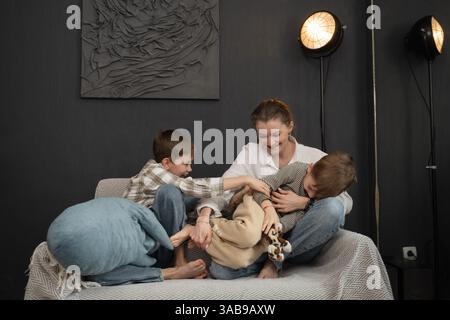 Ein fröhlicher Familienmoment mit einer Mutter und zwei Kindern, die auf einem gemütlichen Sofa in einem stilvollen Wohnzimmer spielen und Wärme und Zweisamkeit in einem Heim veranschaulichen Stockfoto