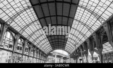 Schwarz-weiß-Foto des großen Innenraums eines historischen Bahnhofs in Nizza, Frankreich, mit atemberaubenden gewölbten Metallrahmen und kompliziertem de Stockfoto