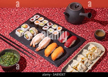 Blick von oben auf ein elegantes Sushi-Abendessen, präsentiert auf einer roten Blumendecke mit dramatischen Schatten Stockfoto