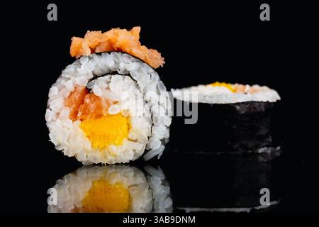 Eine köstliche Sushi-Rolle mit lebendiger Füllung aus Lachs und Mango, auf einer reflektierenden schwarzen Oberfläche. Das schlanke Algen- und Kleberreis-Kontrastmittel bea Stockfoto