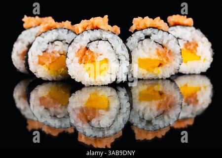 Nahaufnahme von Sushi-Brötchen mit Lachs und Mango auf glänzend schwarzer Oberfläche. Die lebendigen Farben und die komplizierten Texturen spiegeln sich perfekt unten wider. Stockfoto