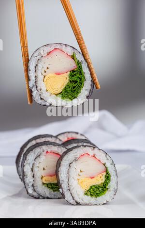 Eine Nahaufnahme von Sushi-Brötchen mit verschiedenen farbenfrohen Zutaten wie Krabben, Omelette und Gemüse, die in Algen und Reis auf weißem Hintergrund gewickelt sind. Hacken Stockfoto