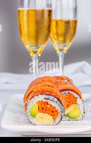 Köstliche Sushi-Brötchen mit Lachs, Avocado und Omelette werden elegant auf einem Teller präsentiert, ergänzt durch zwei Schaumweine im weißen Backgrou Stockfoto