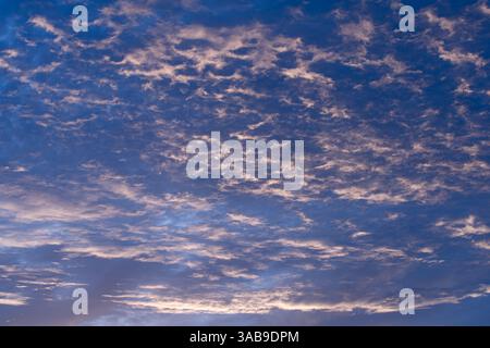 Ein ruhiger Abendhimmel voller weicher, schimmernder Wolken, die von sanften Dämmertönen beleuchtet werden. Der Himmel wechselt von Blau zu sanftem Violett und schafft eine Peak Stockfoto