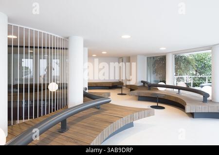 Moderne Einrichtung im Club mit gebogenen Holzbänken und eleganten Eisengeländern. Minimalistisches Design betont offenen Raum und natürliches Licht und schafft so eine besondere Atmosphäre Stockfoto