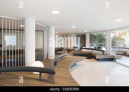 Moderner Raum im Club mit eleganten, geschwungenen Sitzgelegenheiten, runder Beleuchtung und großen Fenstern. Minimalistisches Design betont natürliches Licht und viel Raum Stockfoto