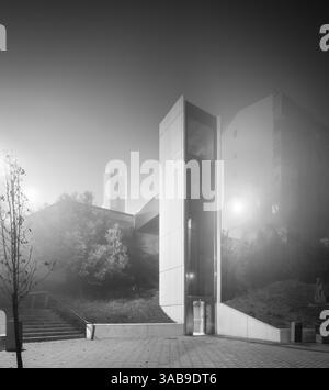 In Nebel und Nebel taucht ein städtischer Aufzug auf, der bei Nacht dezent beleuchtet wird. Das moderne Design steht im Kontrast zur natürlichen Weichheit der nebeligen Umgebung Stockfoto