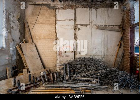 In einem Zimmer, das gerade renoviert wird, sind freiliegende Mauerwerke und Baumaterialien zu sehen. Stapel aus Stahlstäben, Holzdielen und Werkzeugen deuten auf eine laufende Umgestaltung hin Stockfoto