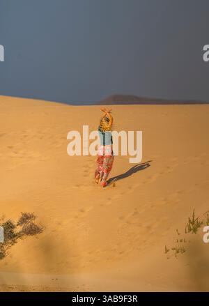 Eine Frau spaziert fröhlich auf den goldenen Sanddünen von Fuerteventura und genießt die Weite der Natur. Ihr farbenfrohes Outfit steht im Kontrast zum ruhigen Ambiente Stockfoto