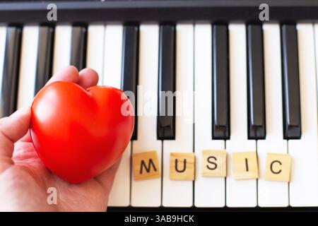 Wortmusik aus Holzwürfeln auf schwarzem und weißem Hintergrund mit Hand, die ein rotes Herz hält. Piano-Oktave aus nächster Nähe von oben. Keybo Stockfoto