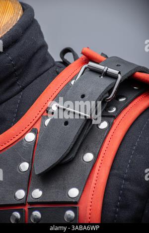 Nahaufnahme der Samurai-Rüstung aus schwarzem Leder. Komplexe Konstruktion mit mehrlagigen Lederplatten mit leuchtend roten Kanten und Metallnieten. Stockfoto