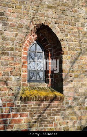 Eine Nahaufnahme eines alten bogenförmigen Kirchenfensters in Tsjaard, Friesland, eingerahmt von Schatten von Baumzweigen. Stockfoto