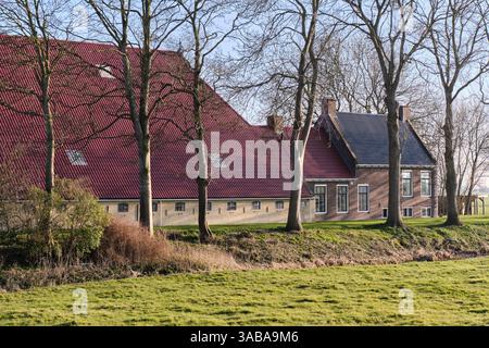 Ein klassisches friesisches EK-hals-Romp (Kopf-hals-Körper) Bauernhaus in der Nähe von Swichum, Niederlande, mit einem großen roten Dach, Ziegelmauern und ländlicher Umgebung Stockfoto