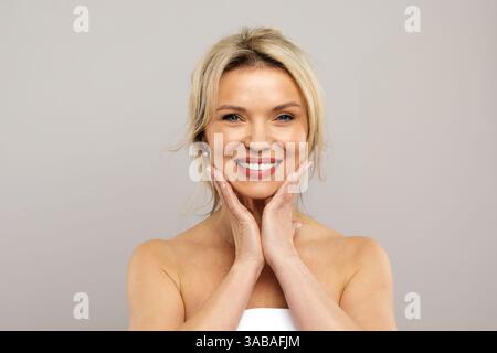 Konzept für Flächeninjektionen. Frau mittleren Alters, in Handtuch gewickelt, berührt ihre Haut Stockfoto