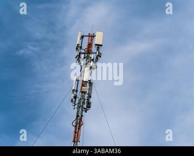 Unteransicht der Oberseite eines hohen Masts mit mobilen Mobilfunkantennen vor blauem Himmel Stockfoto