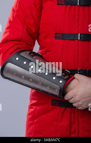 Nahaufnahme der silbernen Schienenkarmbänder auf roter gepolsterter Rüstung. Dieses Bild zeigt eine Nahaufnahme von silbernen Metallschienen, die über einem rot gepolsterten Kleidungsstück getragen werden. Stockfoto
