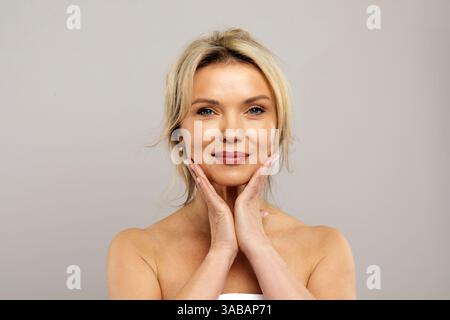 Schöne weiße Frau mittleren Alters, die ihr Gesicht sanft mit beiden Händen berührt Stockfoto