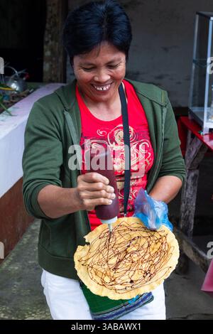 Ein philippinischer Händler lächelt, während er Zuckersirup auf einem Kabkab schüttelt, einem traditionellen, dünnen und knusprigen Süßigkeiten auf Maniok-Basis auf den Philippinen Stockfoto